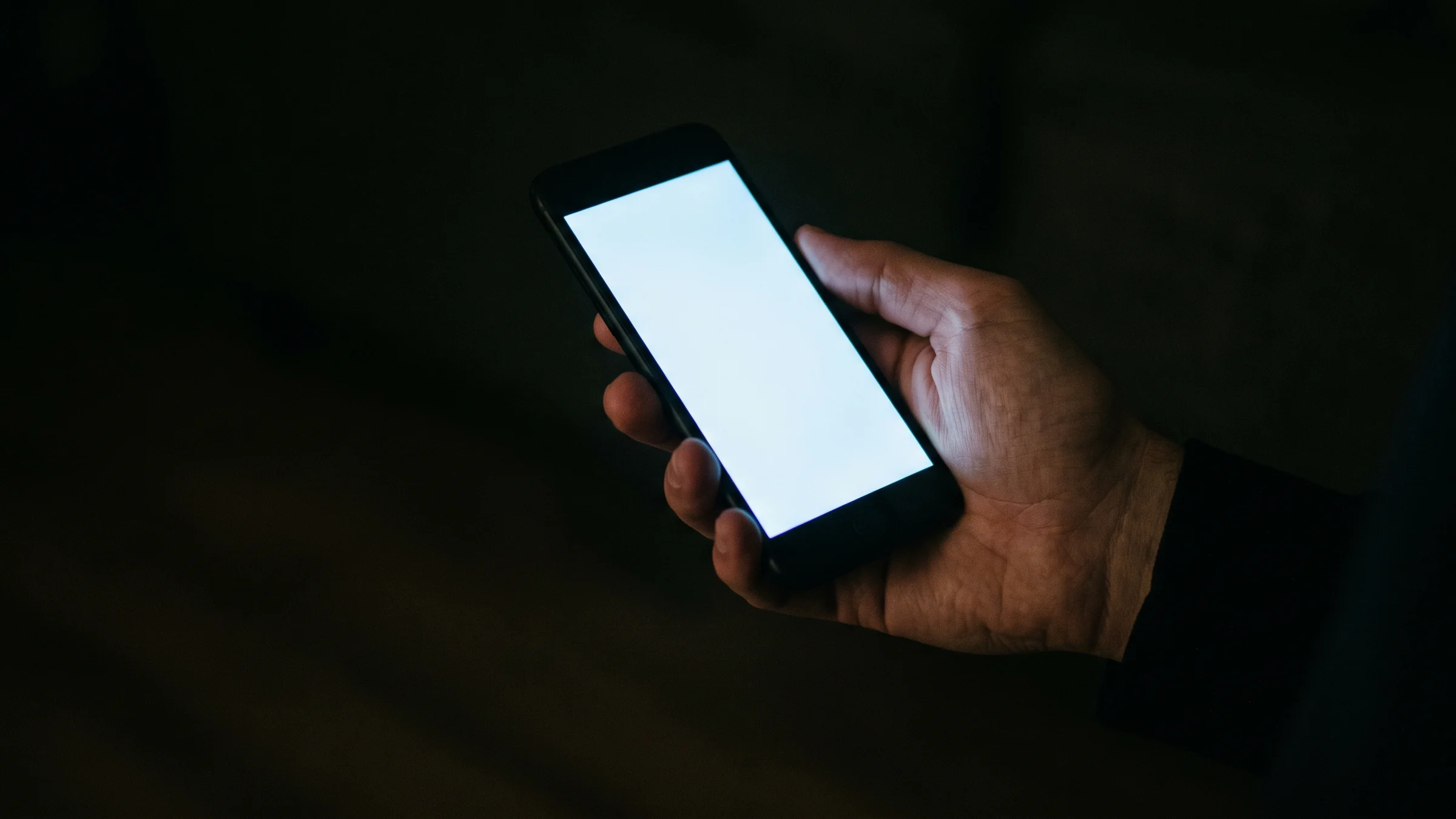 夜、手に持ったスマートフォンの画面の光だけが見えている。